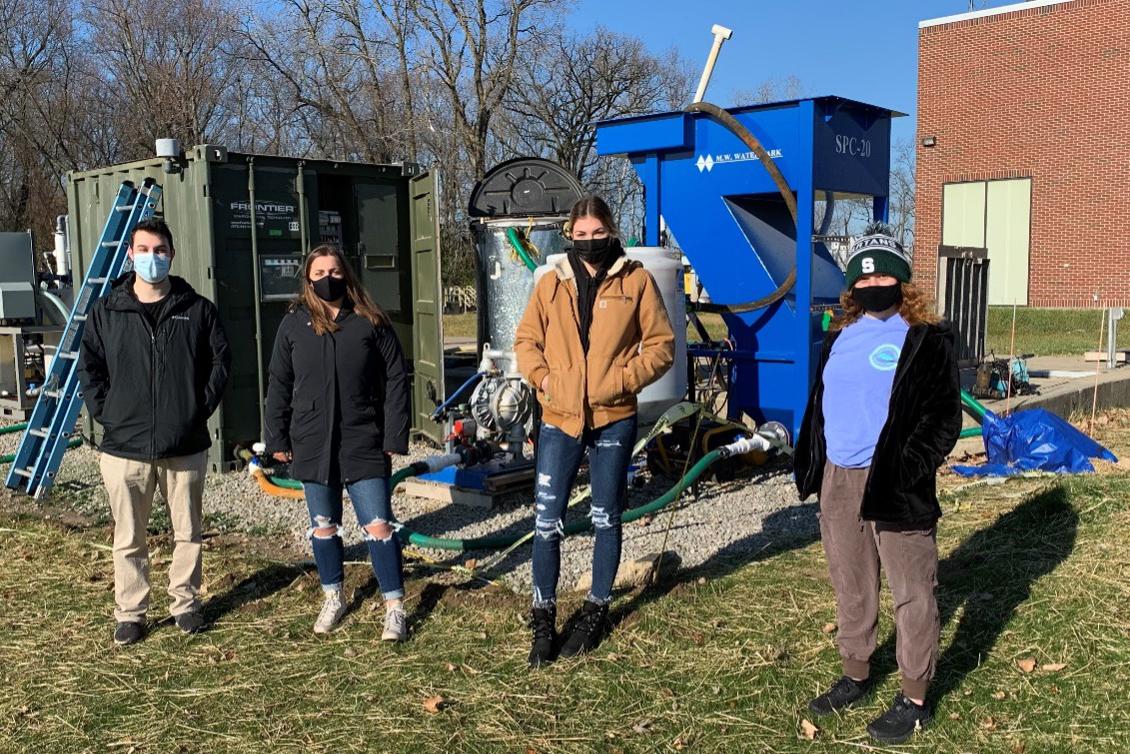 Masked students stand socially distant in front of a wastewater treatment plant