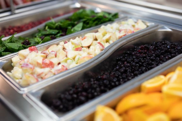 Image of school food offerings in metal pans including brightly colored fruits and vegetables.