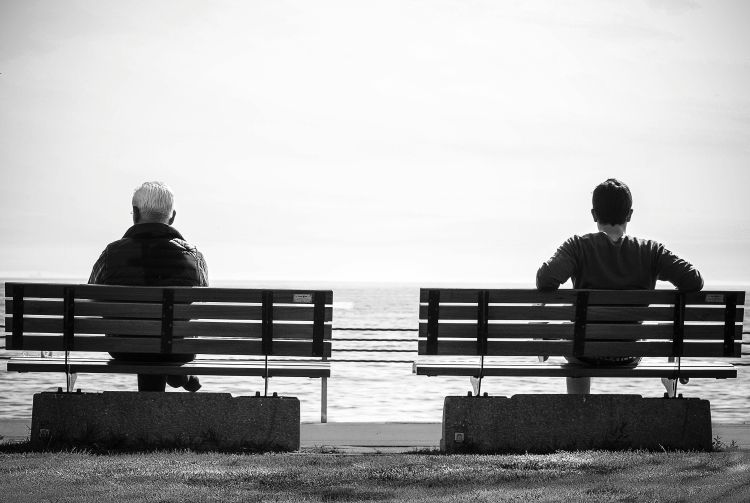 Two people sitting on benches and watching the river.