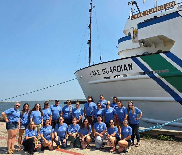 Twenty two people wearing blue shirts form two lines on the dock beside the science vessel Lake Guardian. The group participated in a science workshop.