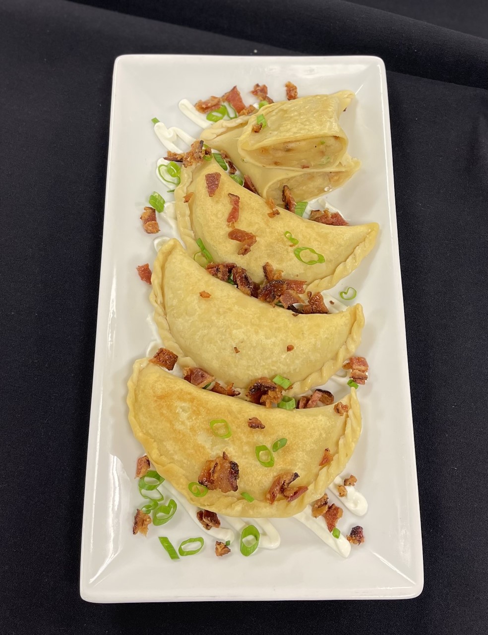 Potato pierogis with toppings displayed on plate.